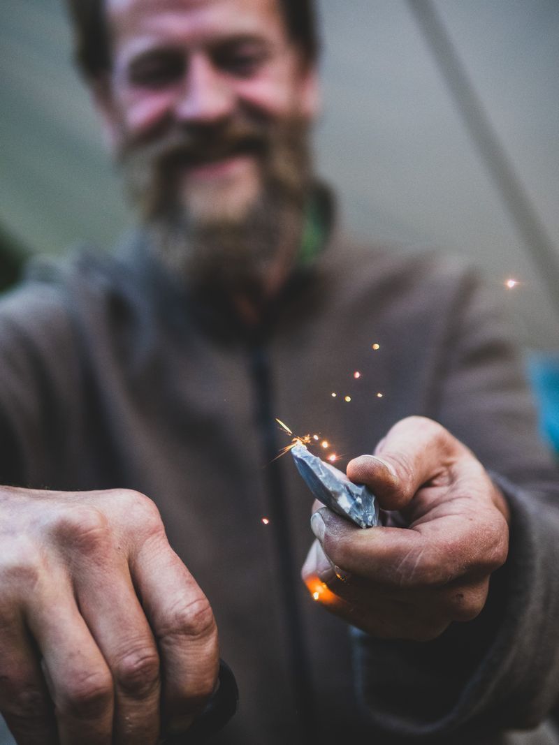 Florian Köhler schlägt mit einem Feuerstein Funken – Nahaufnahme der Hände mit Lächeln im Hintergrund.
