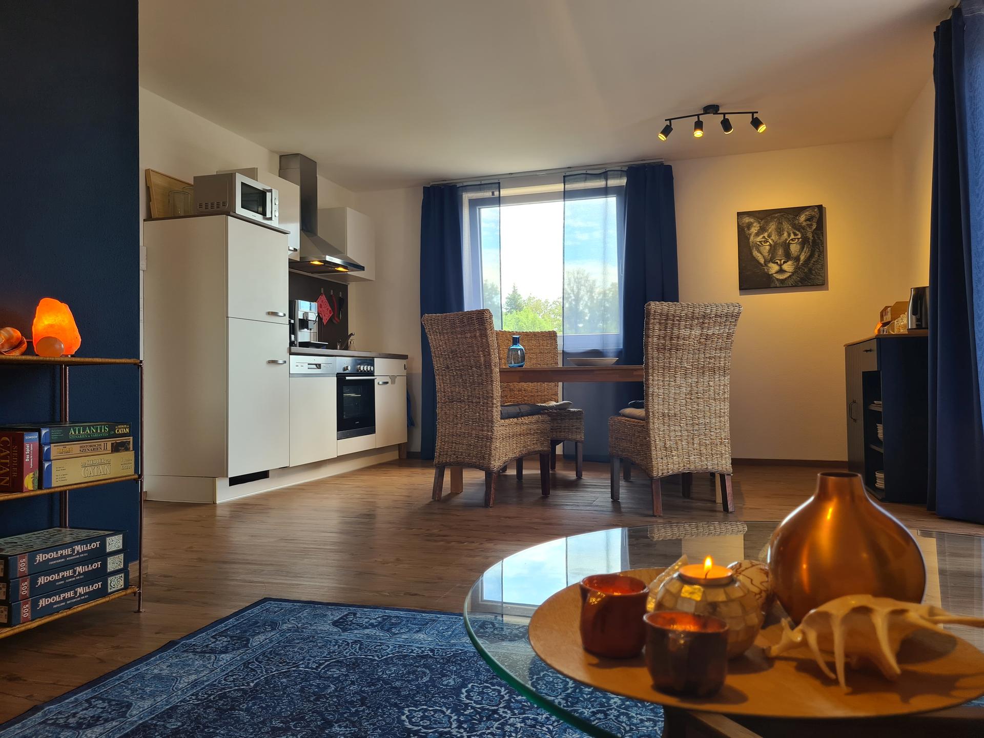 Die gemütliche Wohnküche der Ferienwohnung Perle am Kobernaußerwald mit Deko, Ölbild und Küchenzeile, sowie Esstisch und Stühlen.