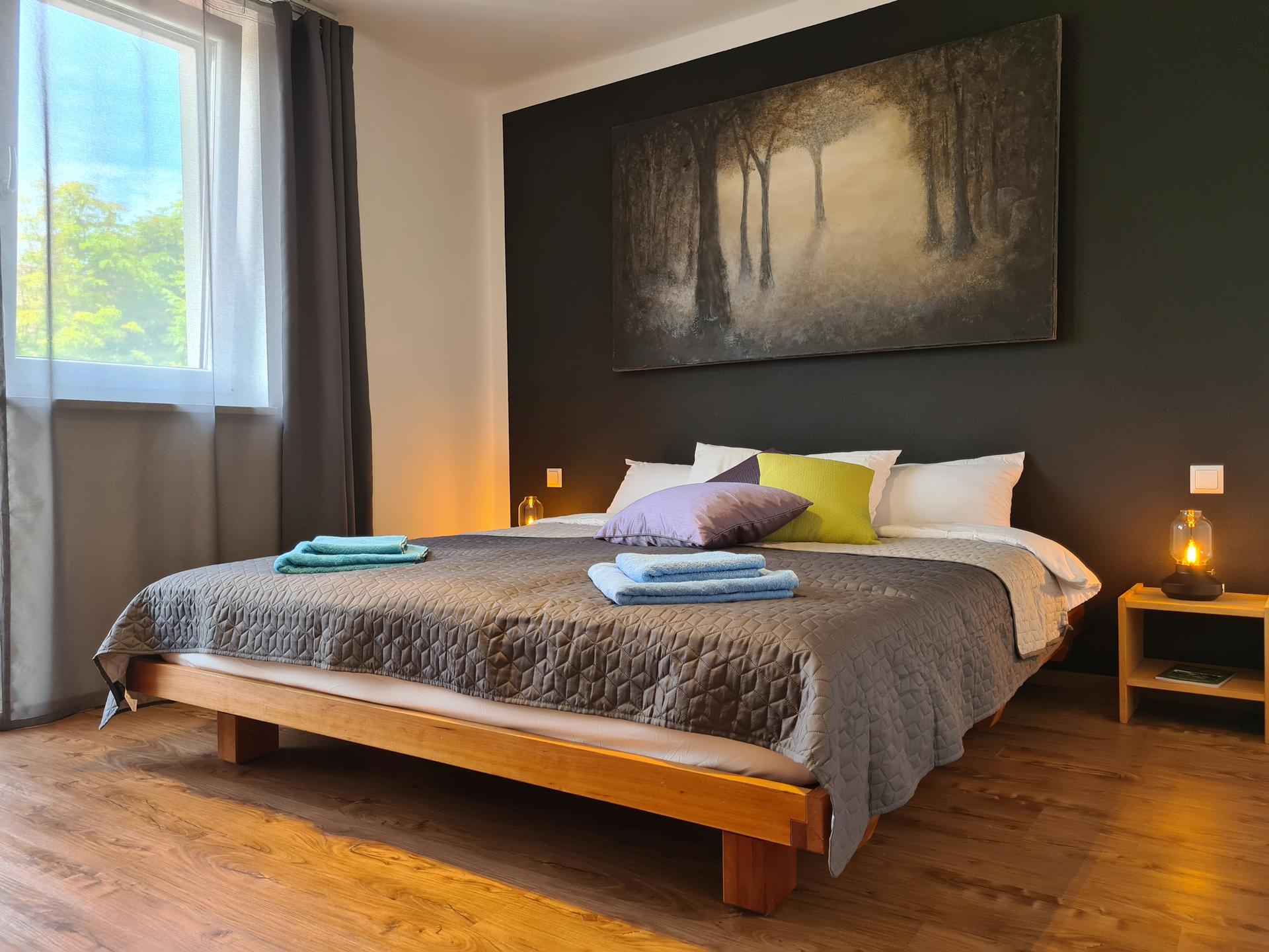 Gemütliches Schlafzimmer mit großem Gemälde an der Wand und massivem Holzbett vom Tischler.