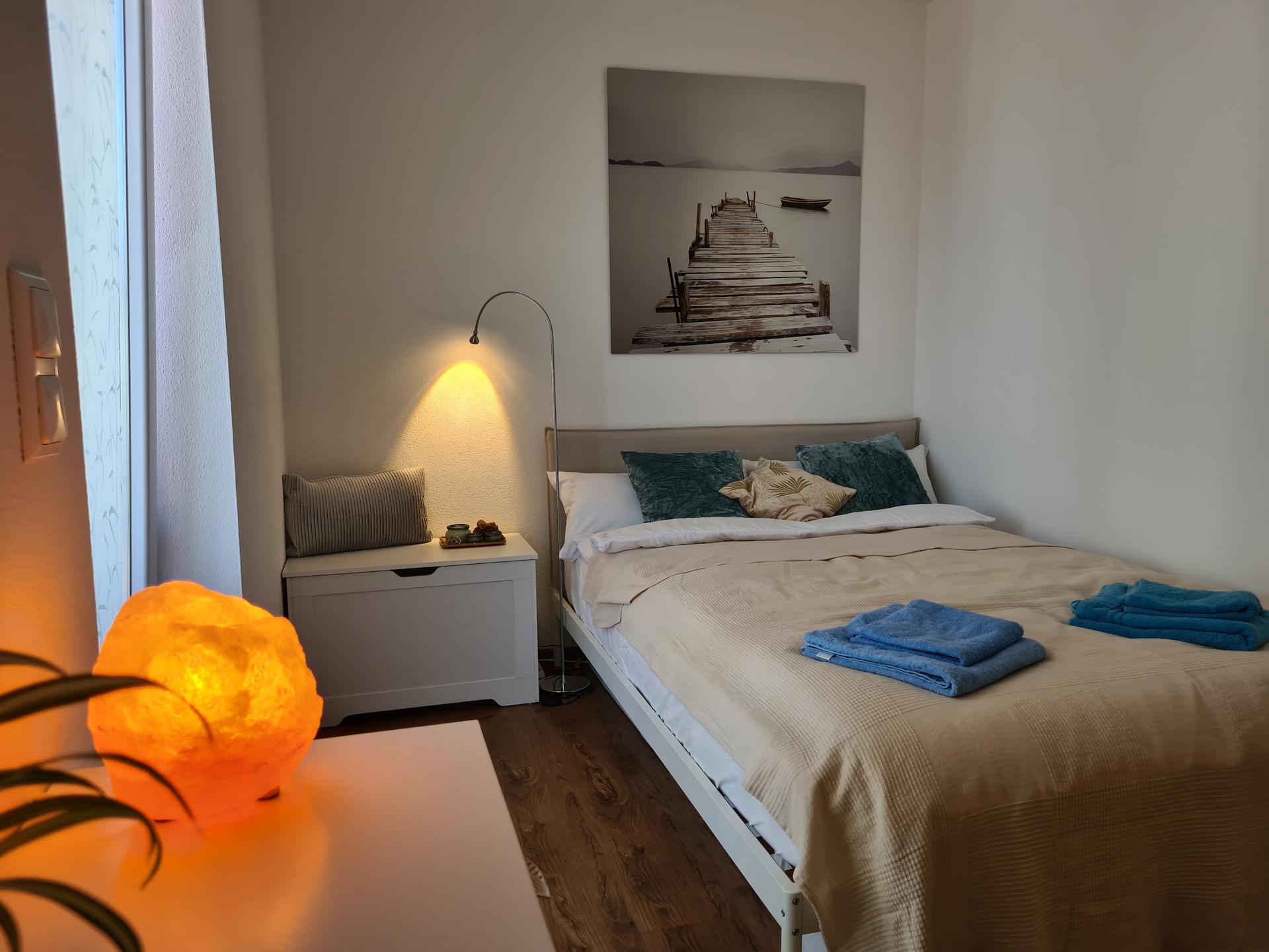 Helles Schlafzimmer mit Salzlampe und Bild an der Wand.