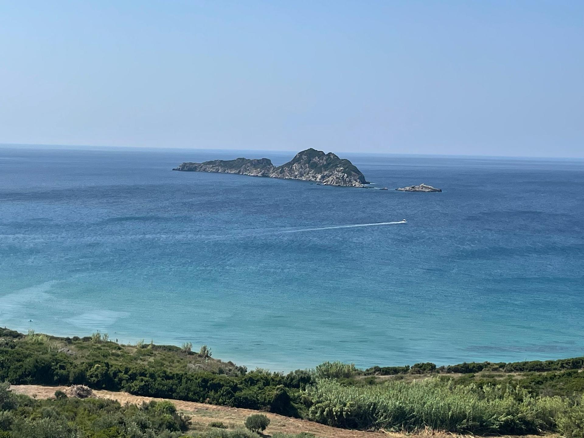 Weitblick auf das offene blaue Meer und die Küste Korfus mit einer kleinen Insel im Hintergrund.